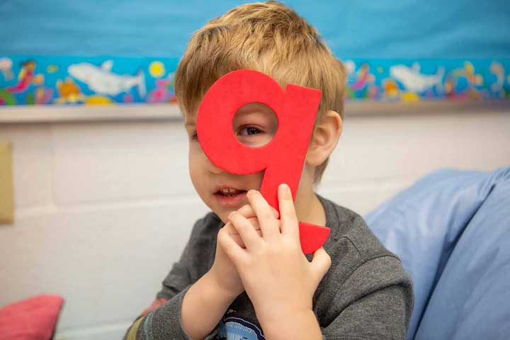 Boy holding the letter Q in front of his eye