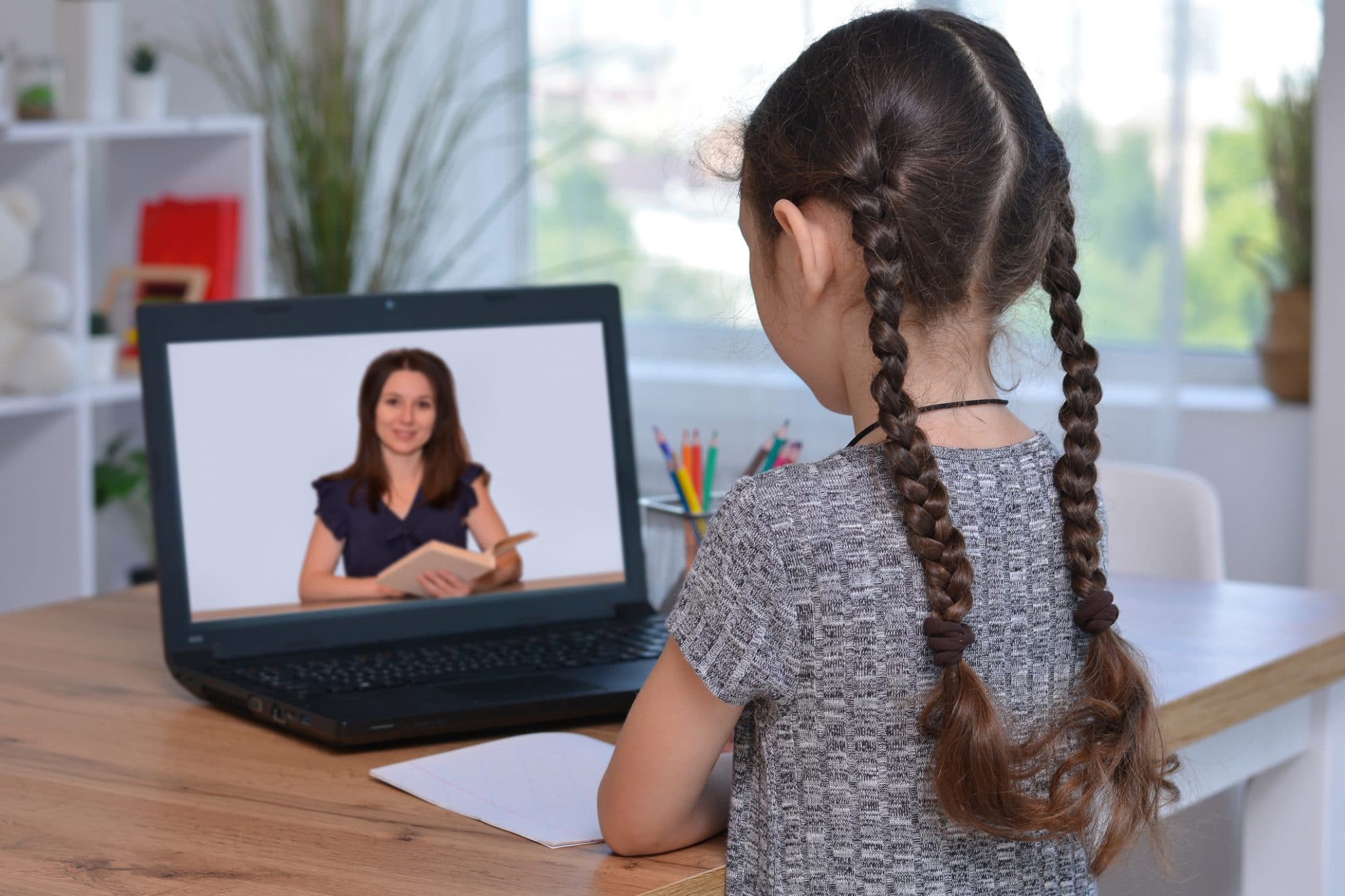 Schoolgirl during quarantine does homework via laptop, listening to the teacher on the monitor screen. Distance home schooling. Online education