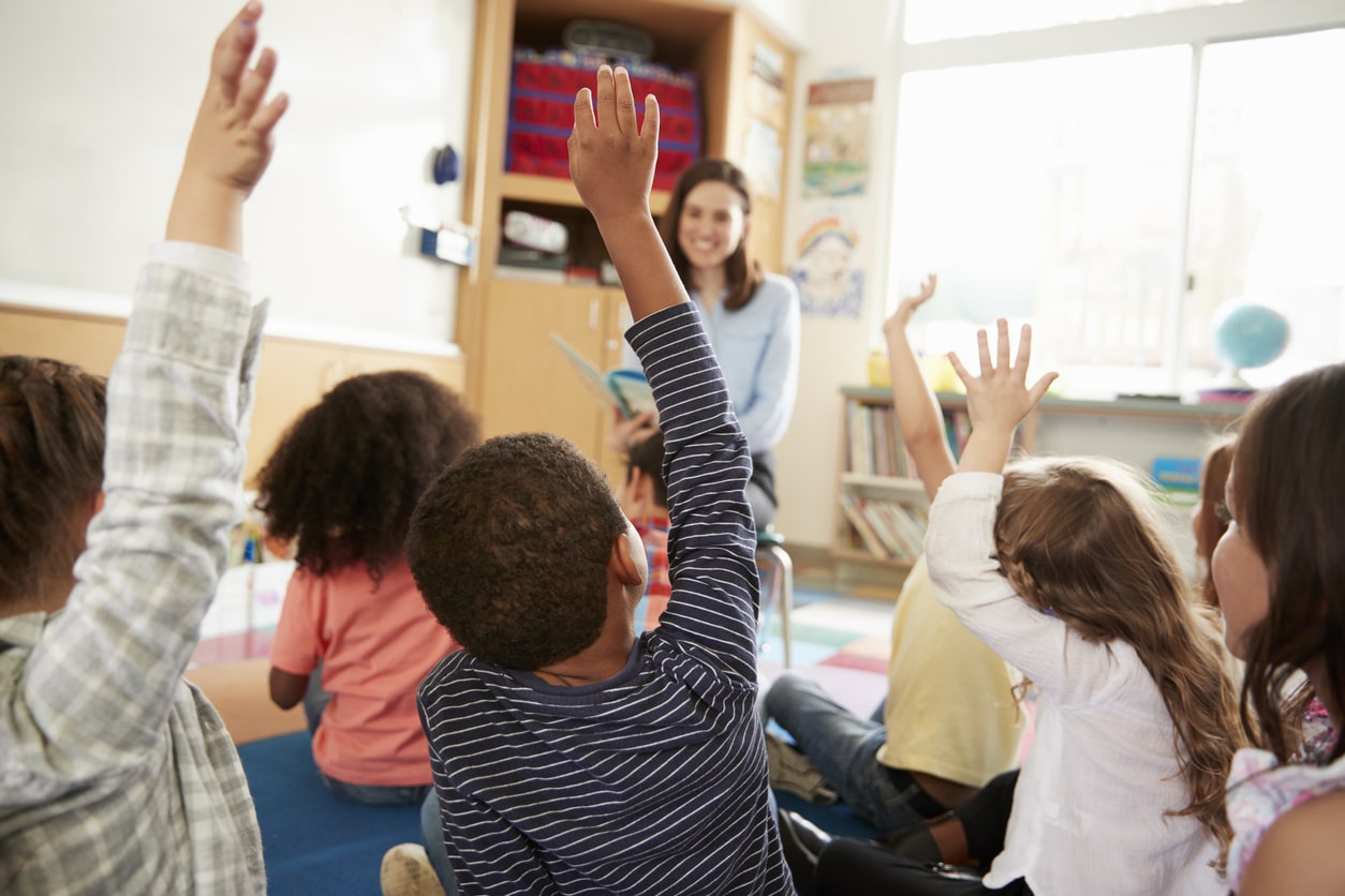 Elementary school kids raising hands to teacher